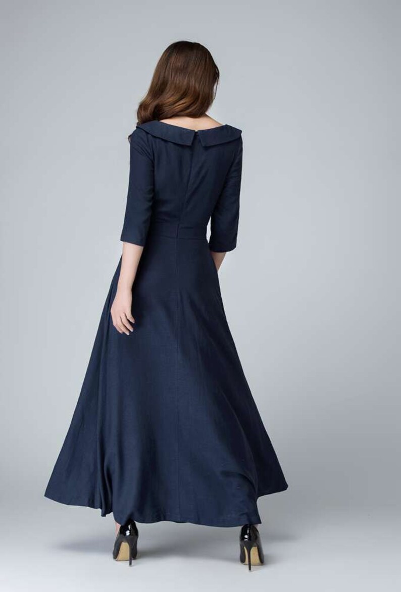 May include: A navy blue maxi dress with a wide, sailor-style collar and three-quarter sleeves. The dress has a fitted bodice and a flowing skirt.