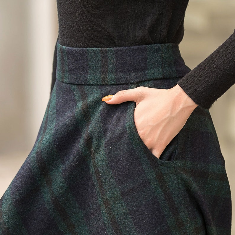 May include: A black and green plaid skirt with a pocket on the right side. The skirt is made of a soft, textured fabric.