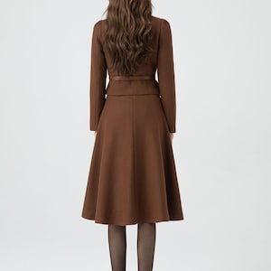 May include: A brown skirt suit with a fitted jacket and a flared skirt. The jacket has a belt at the waist. The skirt is knee-length.