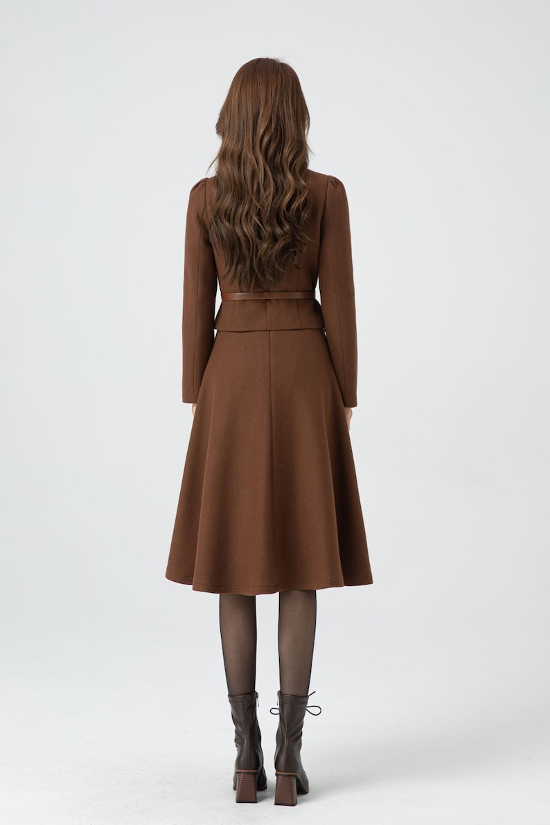May include: A brown skirt suit with a fitted jacket and a flared skirt. The jacket has a belt at the waist. The skirt is knee-length.