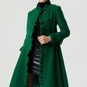 May include: A long, green coat with a ruffled collar and cuffs. The coat has a fitted bodice and a flared skirt. It is buttoned up the front with large, round buttons.
