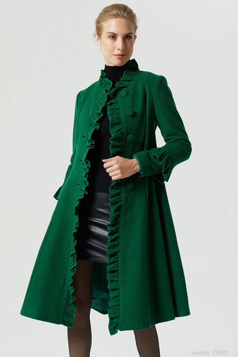 May include: A long, green coat with a ruffled collar and cuffs. The coat has a fitted bodice and a flared skirt. It is buttoned up the front with large, round buttons.