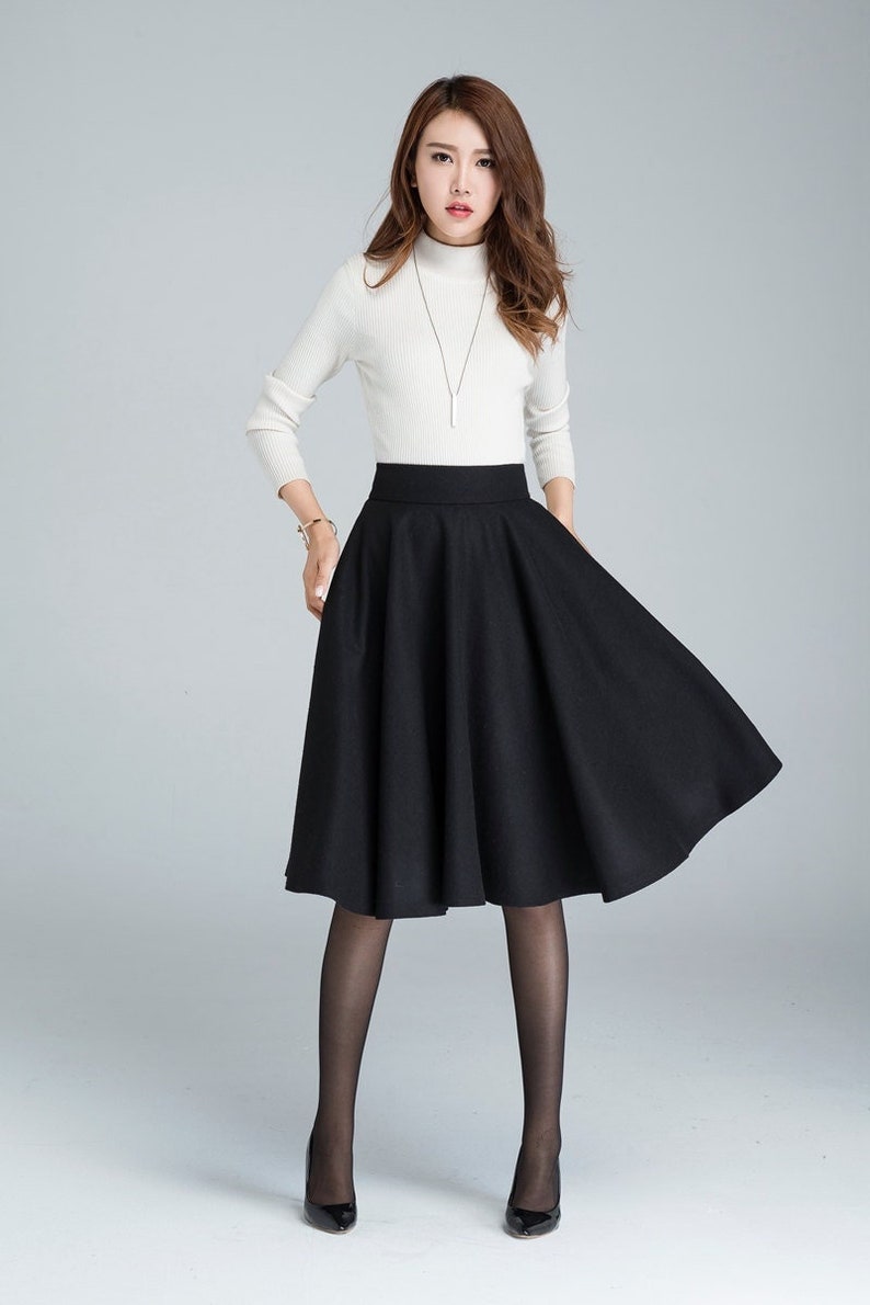 Peut inclure: Une jupe noire &agrave; taille haute avec une silhouette &eacute;vas&eacute;e. La jupe est mi-longue et faite d'un tissu &eacute;pais et textur&eacute;.