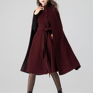 Pu&ograve; includere: Un cappotto a mantella color bordeaux scuro con collo alto a volant, chiusura con bottone perlato, bottoni frontali doppiopetto e cintura in tessuto abbinata in vita. Il capo presenta aperture per le braccia e una linea svasata.