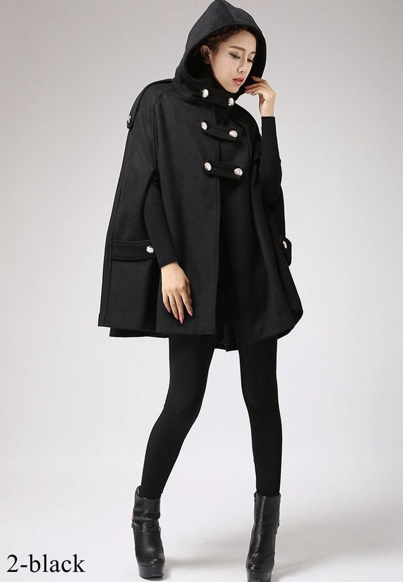 May include: Black hooded cape with a double-breasted button closure and pockets. The cape is made of a soft, warm fabric and has a relaxed fit.