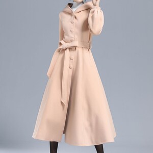 May include: A long, light pink wool coat with a hood, a belt, and button closures. The coat has a flared skirt and long sleeves.