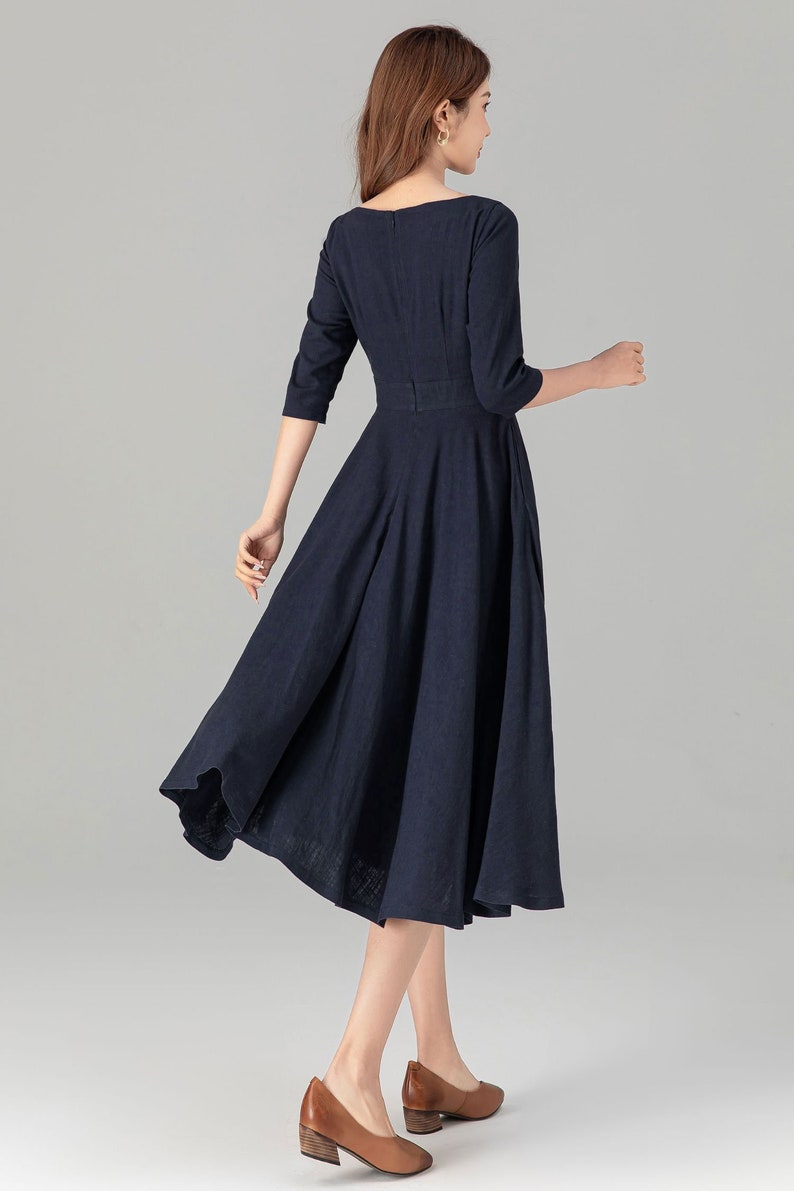 May include: A navy blue midi dress with a boat neckline and a fitted bodice. The dress has a full skirt and is made of a lightweight fabric.