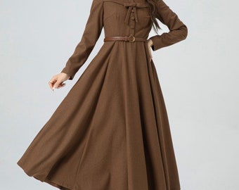 Puede incluir: Un vestido marrón de manga larga con un lazo en el escote y un cinturón marrón. El vestido tiene una falda acampanada y es de largo midi.