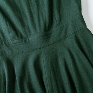 Puede incluir: Un vestido de color verde bosque oscuro que presenta un corpi&ntilde;o ajustado con costuras verticales, una cintura horizontal definida y una falda acampanada. La prenda est&aacute; confeccionada con un tejido texturizado con patrones de tejido visibles.