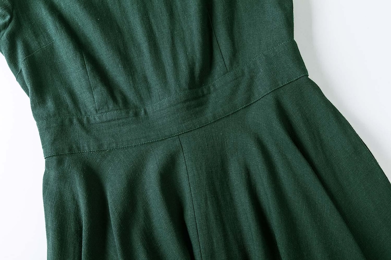 Puede incluir: Un vestido de color verde bosque oscuro que presenta un corpi&ntilde;o ajustado con costuras verticales, una cintura horizontal definida y una falda acampanada. La prenda est&aacute; confeccionada con un tejido texturizado con patrones de tejido visibles.