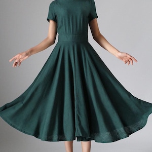 Puede incluir: Un vestido midi de color verde bosque oscuro con mangas cortas, cuello redondo y una cintura ajustada que se abre en una falda amplia y acampanada. La prenda est&aacute; confeccionada con una tela de color s&oacute;lido y llega debajo de la rodilla.