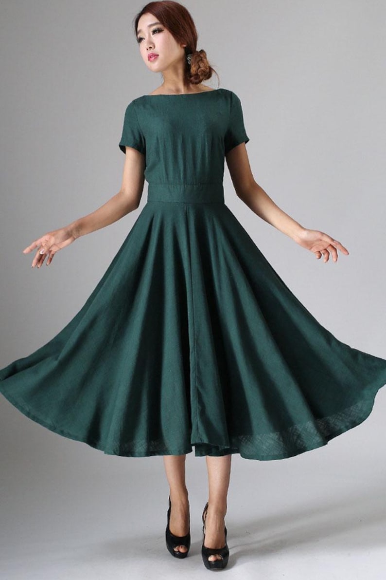 Puede incluir: Un vestido midi de color verde bosque oscuro con mangas cortas, cuello redondo y una cintura ajustada que se abre en una falda amplia y acampanada. La prenda est&aacute; confeccionada con una tela de color s&oacute;lido y llega debajo de la rodilla.