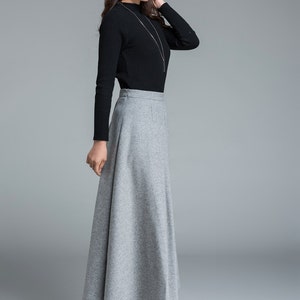 May include: A woman's outfit featuring a black long-sleeved top and a gray, floor-length skirt. The skirt has a flared design. The outfit is paired with black ankle boots. A silver necklace is also visible.