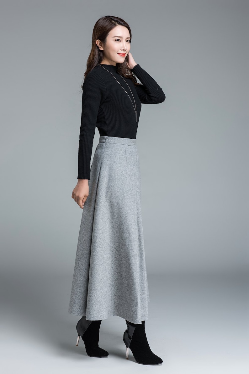 May include: A woman's outfit featuring a black long-sleeved top and a gray, floor-length skirt. The skirt has a flared design. The outfit is paired with black ankle boots. A silver necklace is also visible.