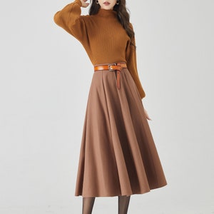 May include: A woman wearing a brown turtleneck sweater with a brown leather belt and a brown midi skirt. She is wearing black tights and black heels.