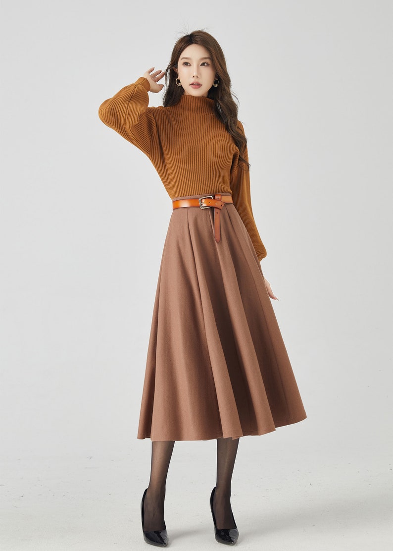 May include: A woman wearing a brown turtleneck sweater with a brown leather belt and a brown midi skirt. She is wearing black tights and black heels.