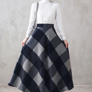 May include: A woman wearing a white long-sleeved blouse and a black and gray plaid skirt. The skirt is a-line and falls to her ankles.