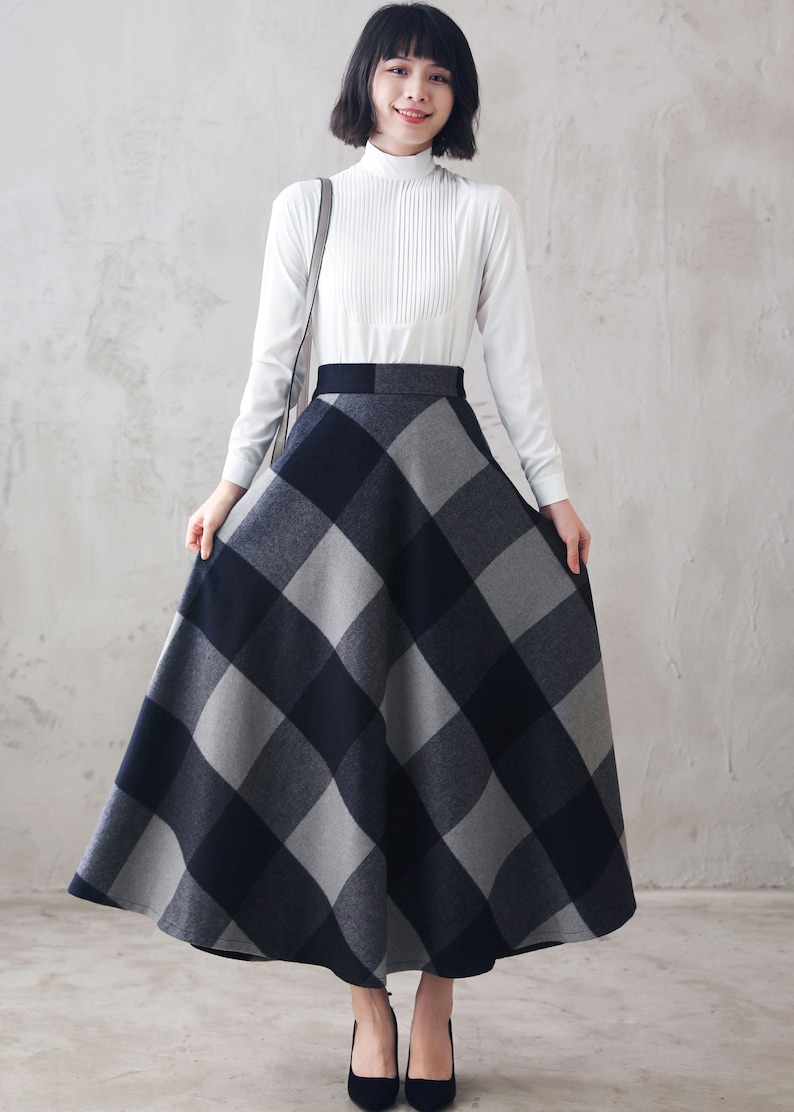 May include: A woman wearing a white long-sleeved blouse and a black and gray plaid skirt. The skirt is a-line and falls to her ankles.