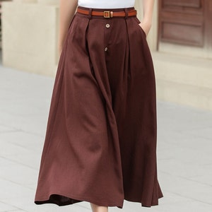 May include: A brown midi skirt with a brown leather belt and a gold buckle. The skirt has a button closure and pleats.