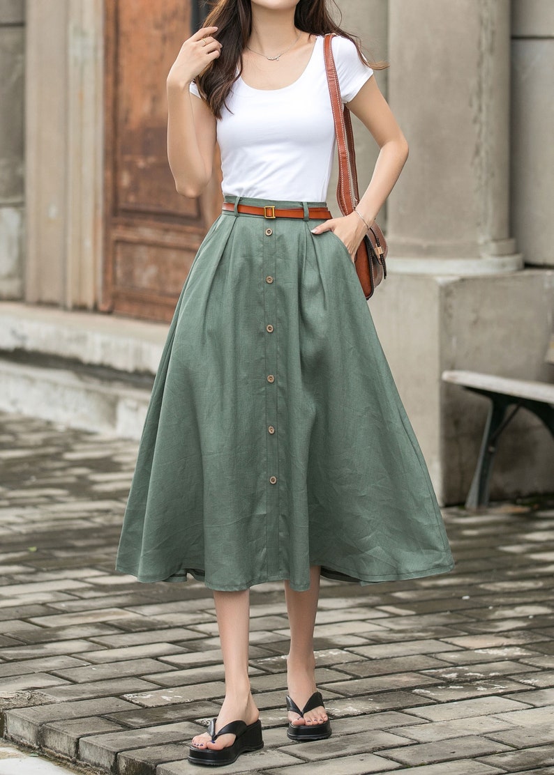May include: A green midi skirt with a button front and a brown belt. The skirt is made of a lightweight fabric and has a flowy silhouette.