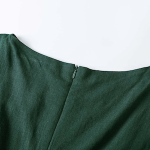 Puede incluir: Una prenda de color verde bosque oscuro con un escote barco ancho y una costura vertical central. Una peque&ntilde;a cremallera oculta, a juego con el color verde, est&aacute; integrada en la costura central trasera para un cierre limpio y sin costuras.