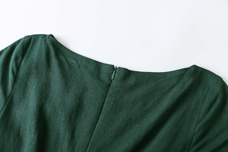 Puede incluir: Una prenda de color verde bosque oscuro con un escote barco ancho y una costura vertical central. Una peque&ntilde;a cremallera oculta, a juego con el color verde, est&aacute; integrada en la costura central trasera para un cierre limpio y sin costuras.