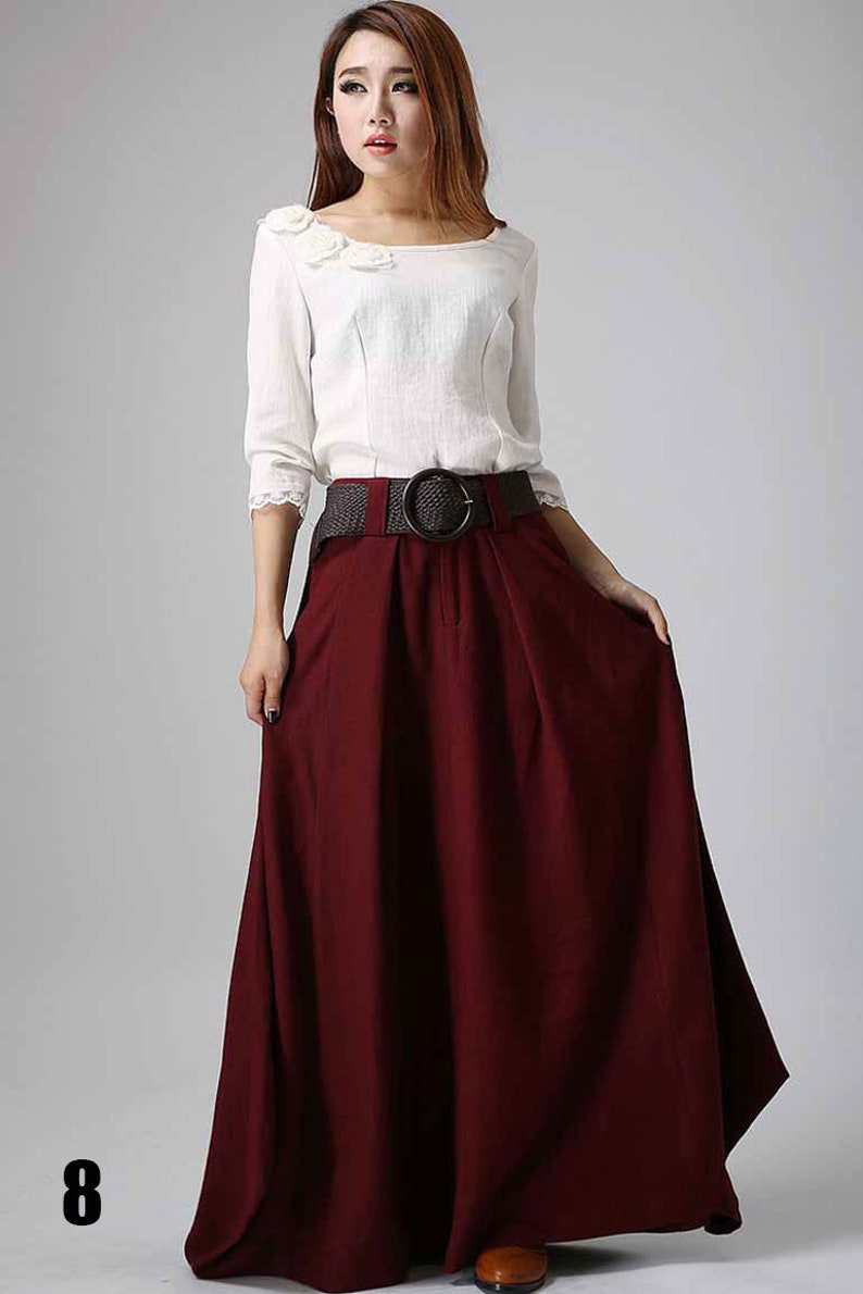 May include: A long, burgundy skirt with a wide brown belt and a large, round buckle. The skirt is made of a soft, flowing fabric and has a simple, elegant design.