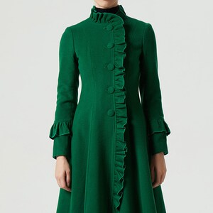 May include: A long, emerald green coat with a ruffled trim down the front and on the sleeves. The coat has a high collar and a button closure.