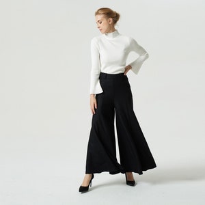 May include: A woman wearing a white turtleneck sweater and black wide-leg pants with a flared hem.