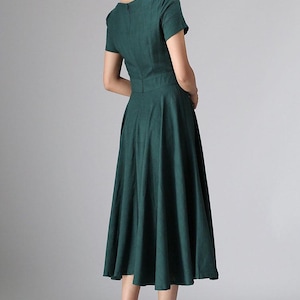 Puede incluir: Un vestido midi de color verde oscuro con mangas cortas, un corpi&ntilde;o ajustado con cintura definida y una falda acampanada que cae por debajo de las rodillas. La prenda incluye un cierre de cremallera oculto en la espalda y un escote redondo sencillo.