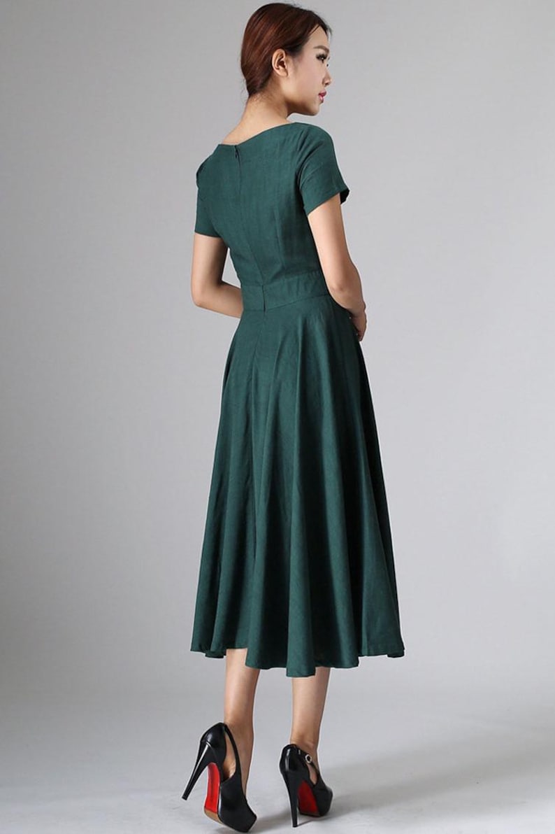 Puede incluir: Un vestido midi de color verde oscuro con mangas cortas, un corpi&ntilde;o ajustado con cintura definida y una falda acampanada que cae por debajo de las rodillas. La prenda incluye un cierre de cremallera oculto en la espalda y un escote redondo sencillo.