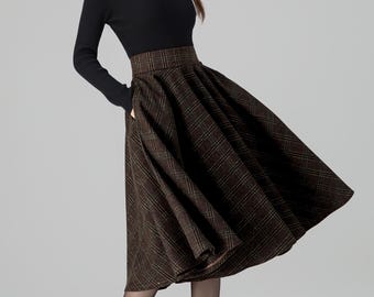 May include: A woman wearing a black long-sleeved sweater and a brown plaid skirt. The skirt is knee-length and has a full, flowing shape. She is also wearing black tights and black high heels. The outfit is suitable for fall or winter.