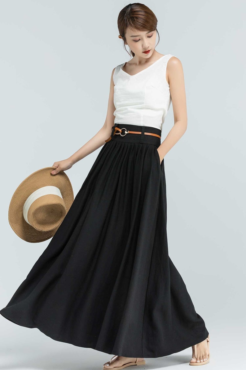 May include: A black maxi skirt with a brown leather belt and a silver buckle. The skirt has pleats and a flowing silhouette.