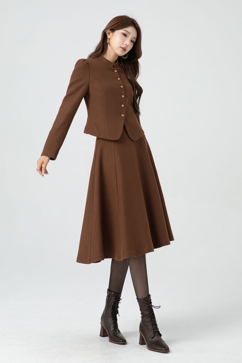 May include: A brown skirt suit with a fitted jacket and a flared skirt. The jacket has a mandarin collar and gold buttons. The skirt is knee-length and has a slight A-line shape.
