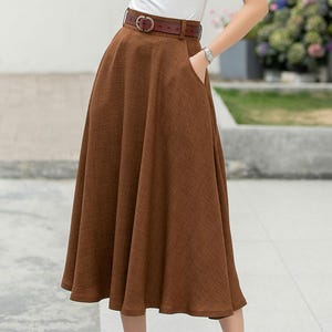 May include: A brown midi skirt with a brown leather belt. The skirt has a flared silhouette and a simple design.