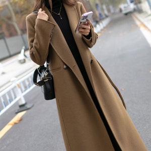 May include: A long brown double-breasted coat with a belt. The coat has a classic style and is made of a soft, warm fabric.