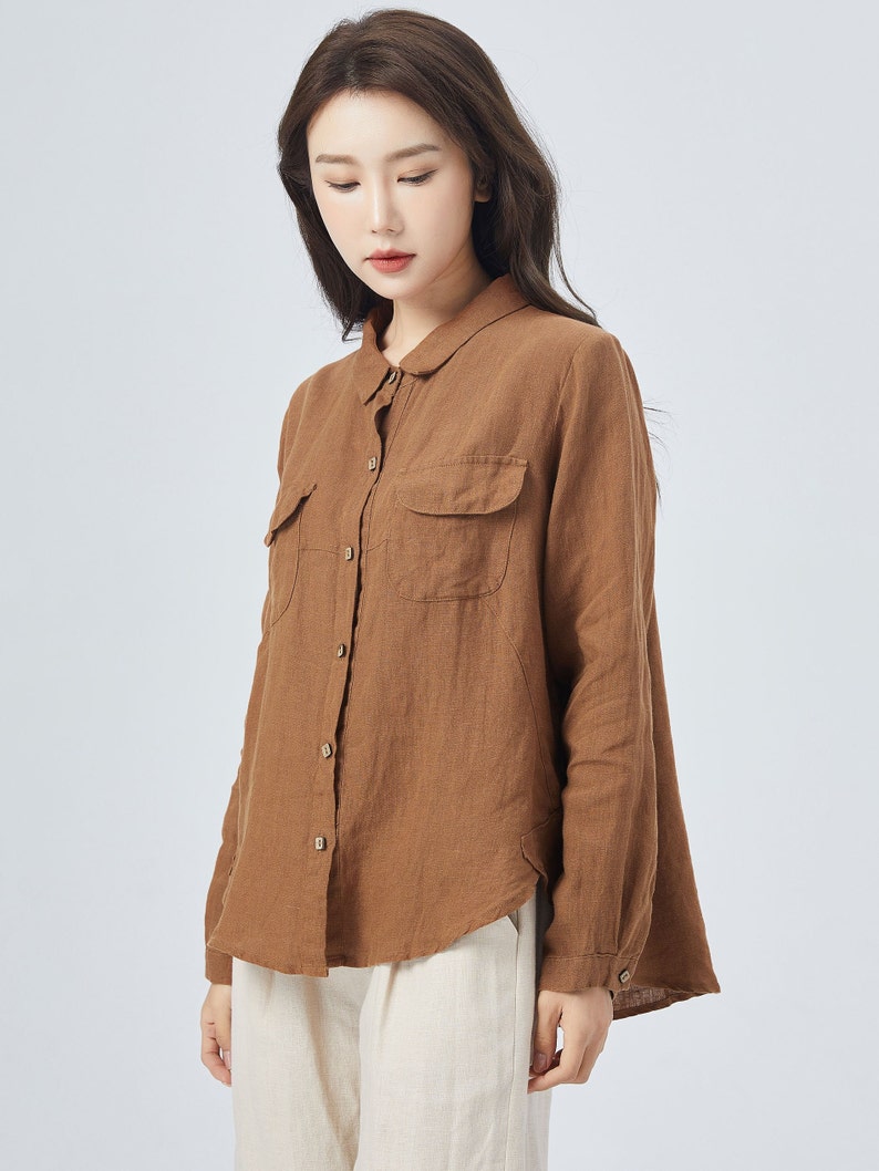 May include: A brown linen shirt with long sleeves, a button-down front, and two patch pockets. The shirt has a relaxed fit and a slightly curved hem.