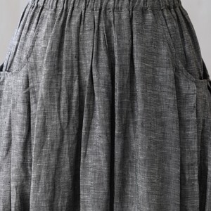 May include: A gray linen skirt with a wide elastic waistband and two pockets on the sides. The skirt is pleated and has a textured, woven look.