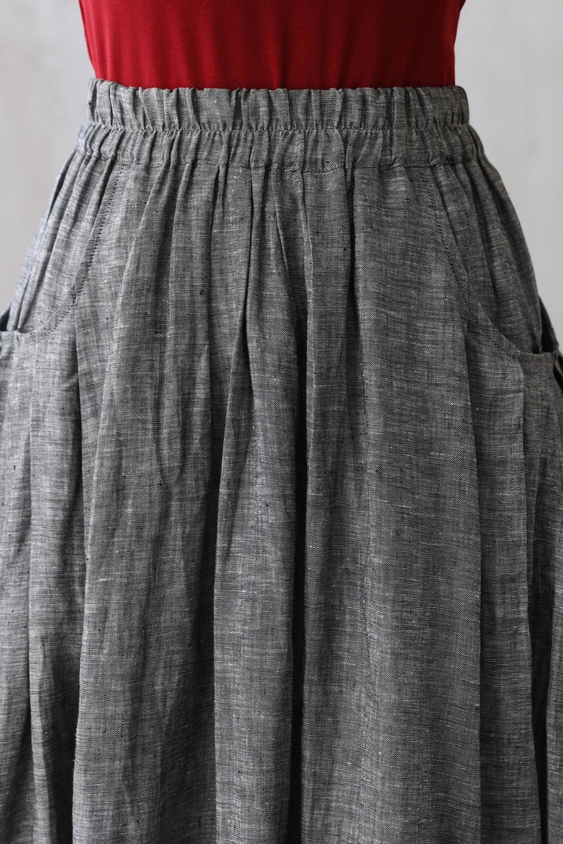 May include: A gray linen skirt with a wide elastic waistband and two pockets on the sides. The skirt is pleated and has a textured, woven look.