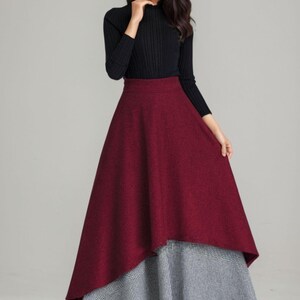 K&ouml;nnte beinhalten: Ein burgunderfarbener und schwarzer Midirock mit hoher Taille und einem geschichteten Design. Der Rock ist aus einem dicken, strukturierten Stoff gefertigt und hat eine leicht ausgestellte Silhouette.