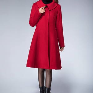 May include: A red wool coat with a wide collar and a flared skirt. The coat is buttoned up the front and has long sleeves.