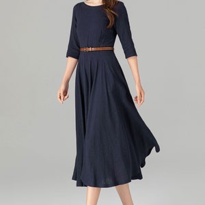 May include: A navy blue midi dress with a brown belt. The dress has a round neckline and 3/4 sleeves. The model is wearing brown heeled shoes.