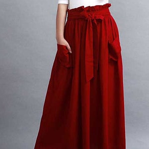 May include: A high-waisted, red skirt with a matching tie belt and pockets. The skirt is paired with a white top. The skirt is a solid color and appears to be made of a lightweight fabric.