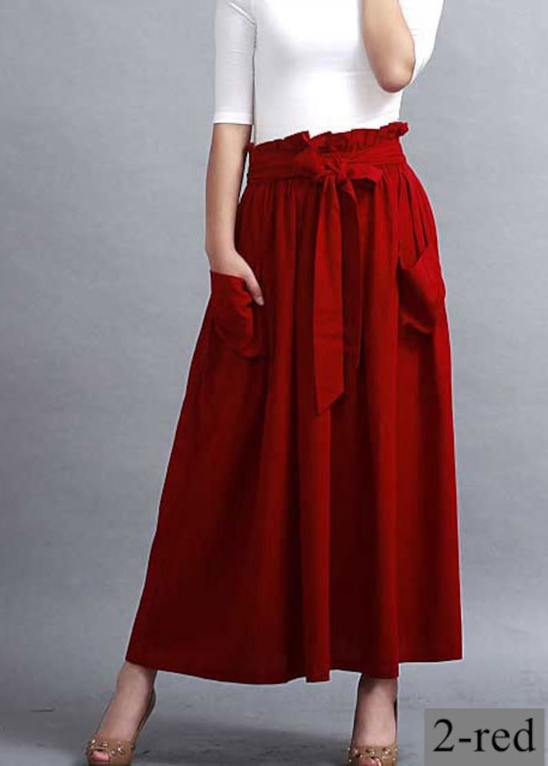 May include: A high-waisted, red skirt with a matching tie belt and pockets. The skirt is paired with a white top. The skirt is a solid color and appears to be made of a lightweight fabric.