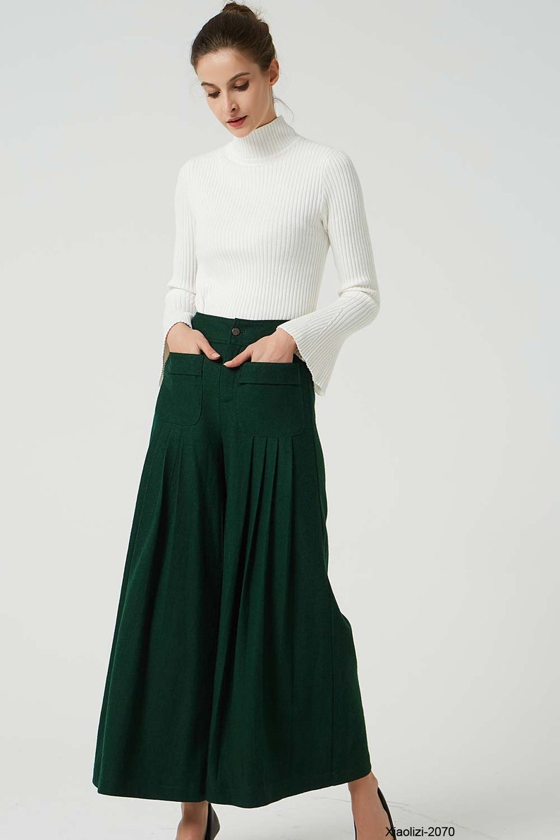 May include: A woman wearing a white turtleneck sweater and dark green wide-leg trousers with pleats and large pockets.