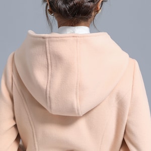 May include: A pale pink hooded coat with a long, fitted silhouette. The coat is made of a soft, plush fabric and has a smooth, even texture.
