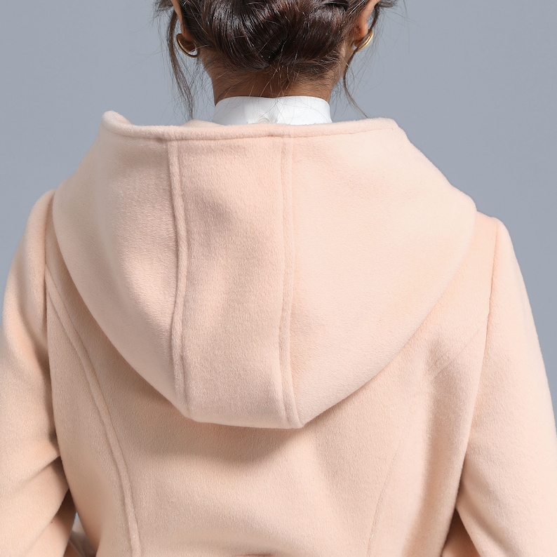 May include: A pale pink hooded coat with a long, fitted silhouette. The coat is made of a soft, plush fabric and has a smooth, even texture.
