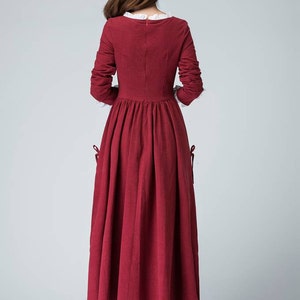 May include: A long-sleeved, burgundy dress with a white lace collar and cuffs. The dress has a fitted bodice and a full skirt. The dress is made of a soft, flowing fabric.