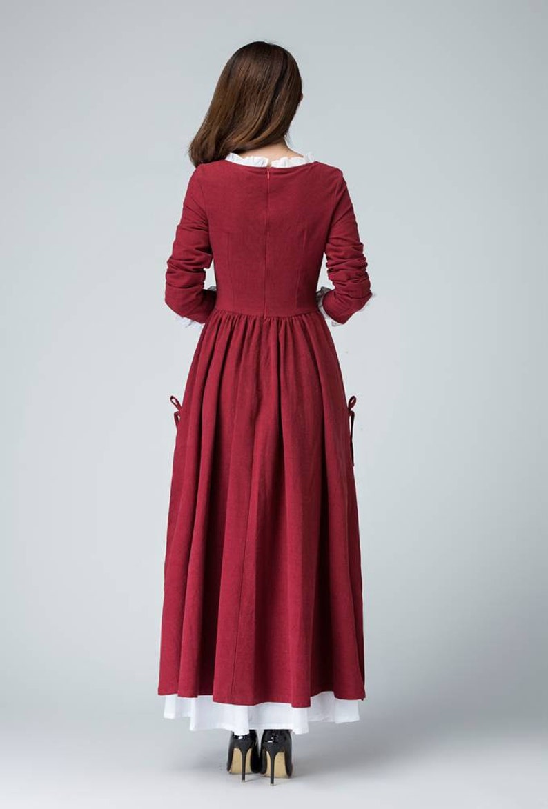 May include: A long-sleeved, burgundy dress with a white lace collar and cuffs. The dress has a fitted bodice and a full skirt. The dress is made of a soft, flowing fabric.