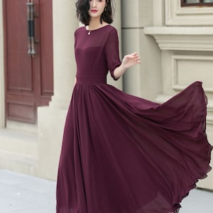 May include: A long, flowing burgundy maxi dress with a round neckline and 3/4 sleeves. The dress has a fitted bodice and a flowing skirt.